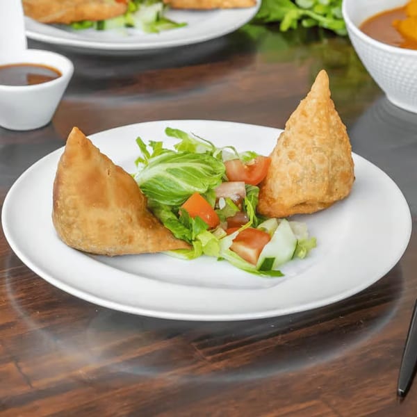 Two golden-brown samosas with a fresh side salad of lettuce, tomatoes, and cucumbers on a white plate.